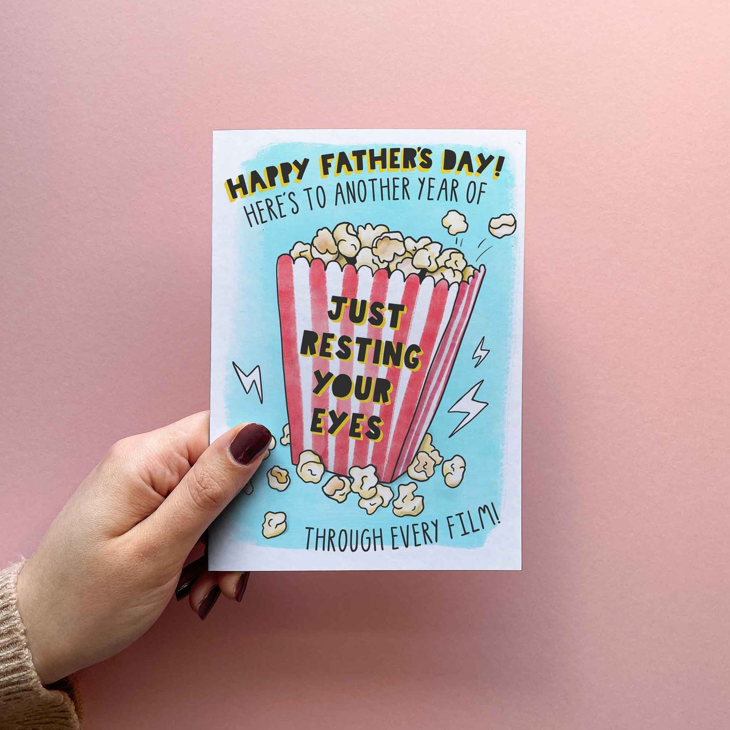 Funny Fathers Day card for Dad, reading: "Happy Fathers Day! Here's to another year of just rising your eyes through every film!" Featuring a popcorn illustration in blue red and yellow.