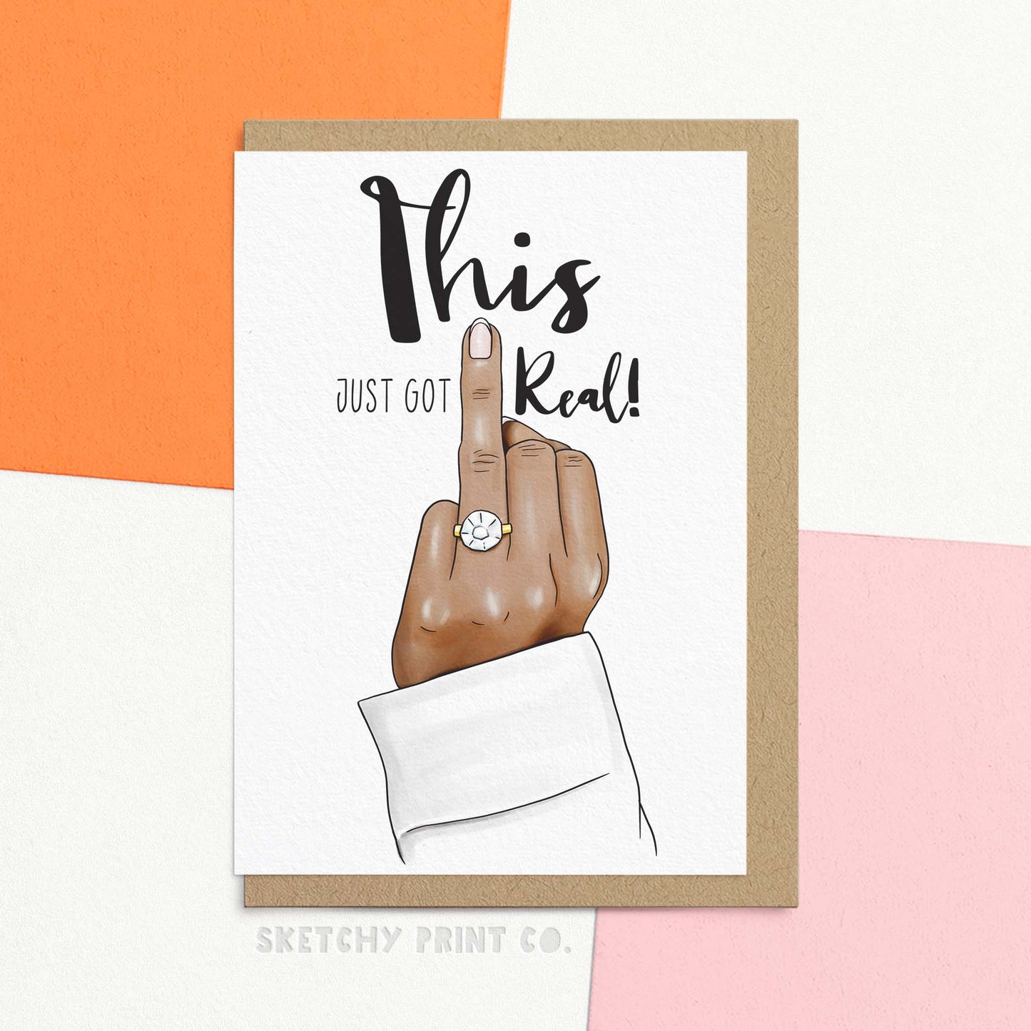 Funny wedding wishes and engagement greetings card reading 'This just got real!' featuring a hand holding up the ring finger showing off a sparkly engagement ring. A hand is holding the card for size reference.